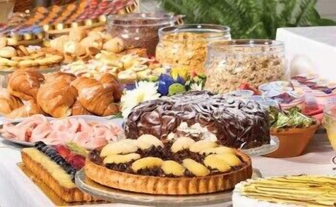 Un bufé con diversos alimentos, incluyendo pasteles, un pastel bañado en chocolate y una variedad de frutas y verduras.