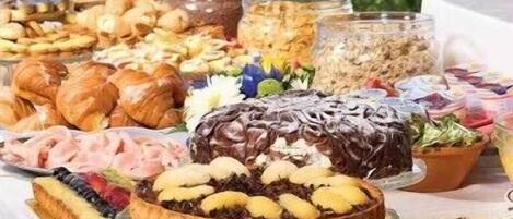 Un bufé con diversos alimentos, incluyendo pasteles, un pastel bañado en chocolate y una variedad de frutas y verduras.