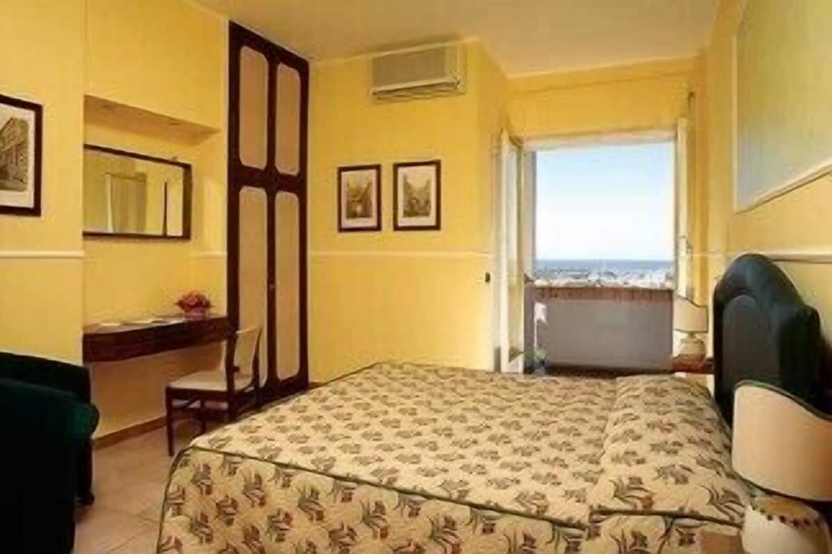 A hotel room with a bed, a desk, a chair, and a window with a view.