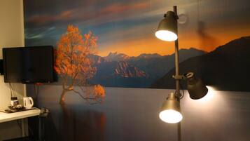 A room with a mountain landscape mural, a desk with a computer, and a desk lamp.