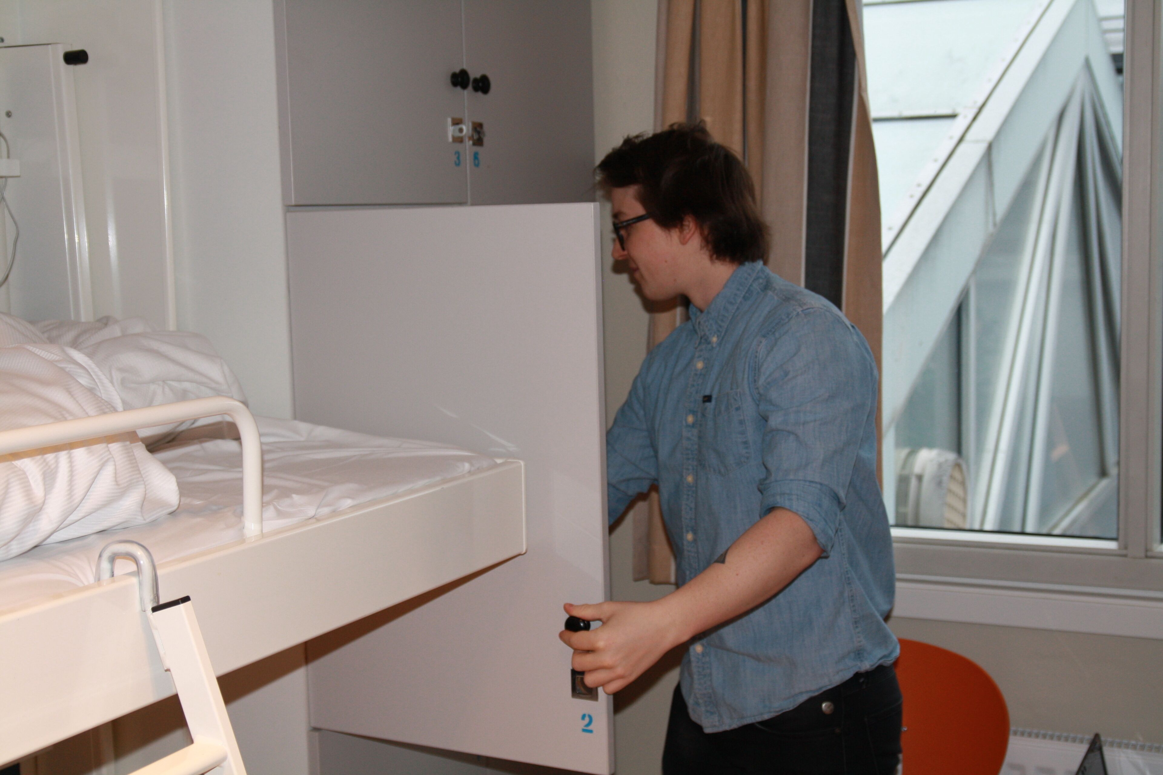 A person opening a door to a room with a bunk bed and a window.