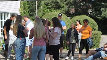 Um grupo de pessoas reunidas ao ar livre, possivelmente num pátio ou espaço público com vegetação e um edifício ao fundo.
