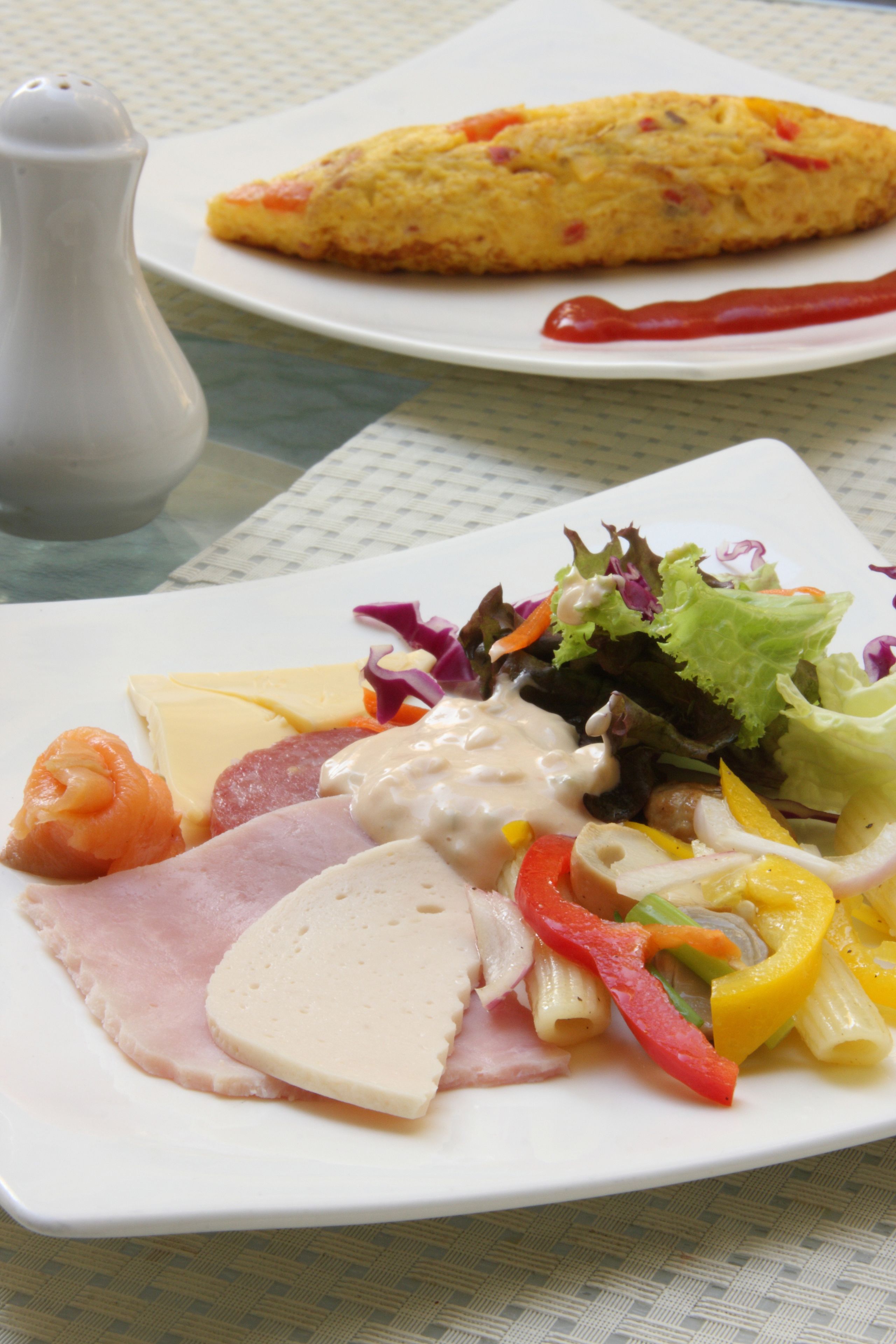 A plate of food with various items including a slice of ham, cheese, and a salad with vegetables and a creamy dressing.