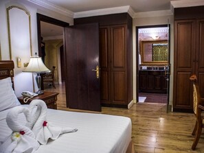 A hotel room with a bed, a bedside table with a lamp, a mirror, and a door leading to a kitchen area. - Four Seasons Place (Pattaya)