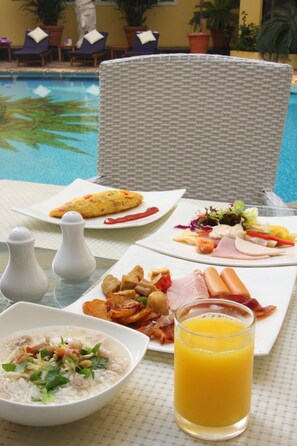 A dining table with breakfast items including eggs, bacon, and a salad, near a poolside setting. - Four Seasons Place (Pattaya)
