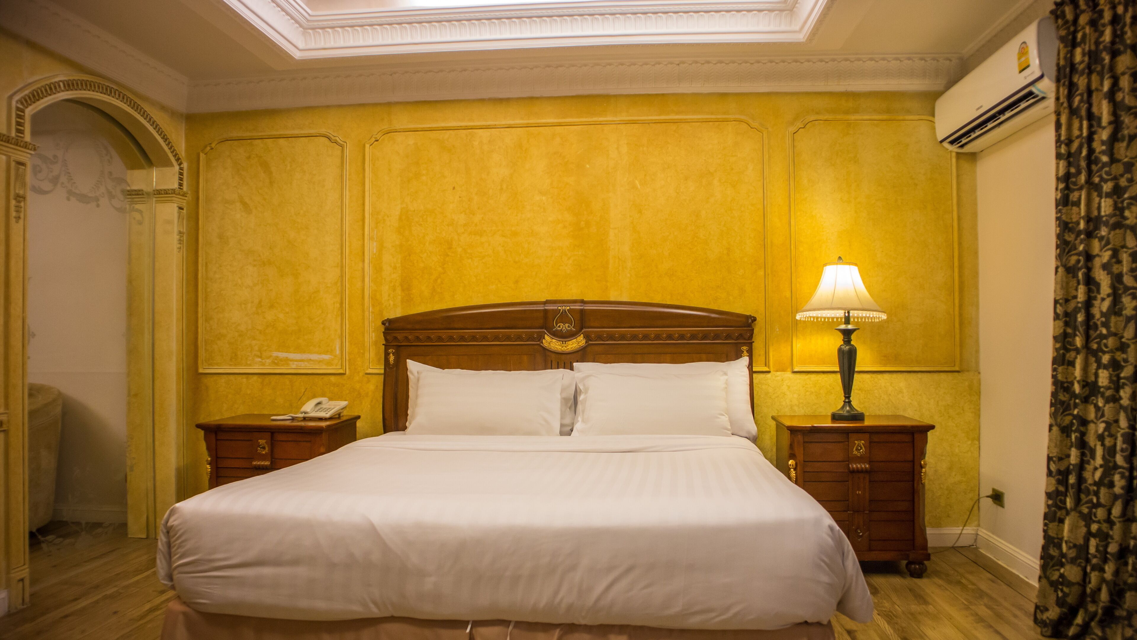 Una cama grande con cabecera de madera, dos mesitas de noche con lámparas, y un teléfono en una de ellas.
