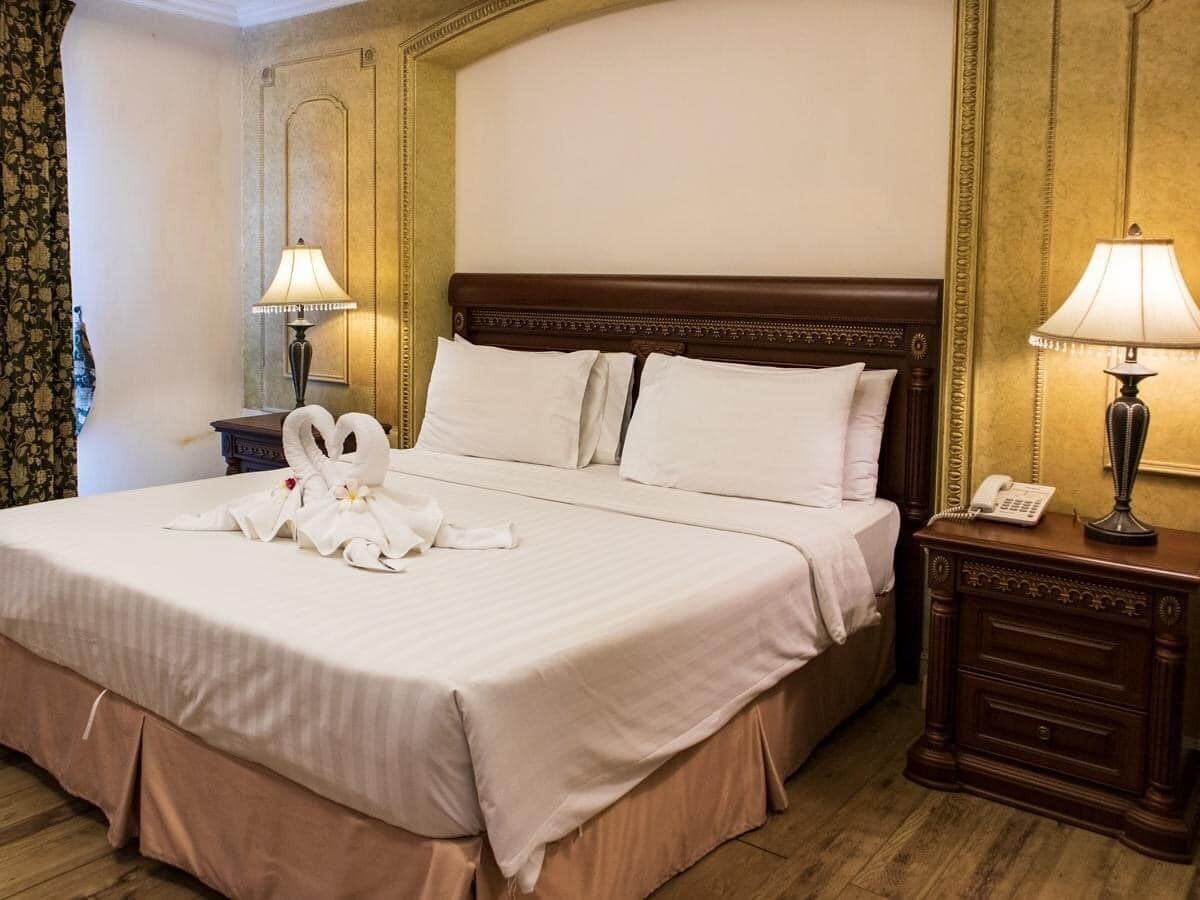 A hotel room with a large bed, two bedside lamps, a wooden nightstand, and a telephone.