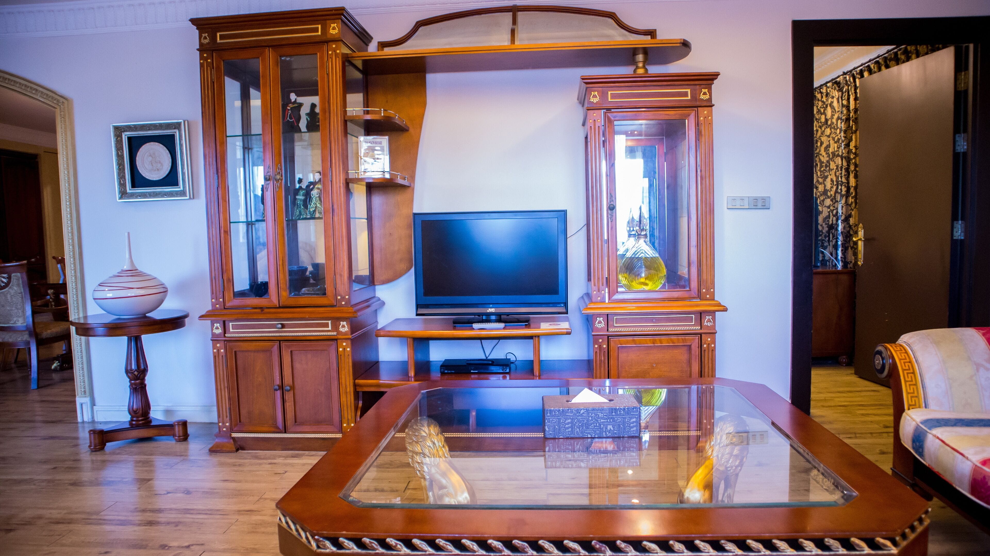 Een woonkamer met een houten tv-meubel, een flatscreentelevisie en een salontafel met een glazen blad.