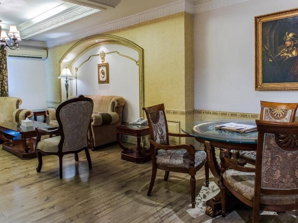 A traditional living room with a round coffee table, two armchairs, a sofa, and a decorative mirror.