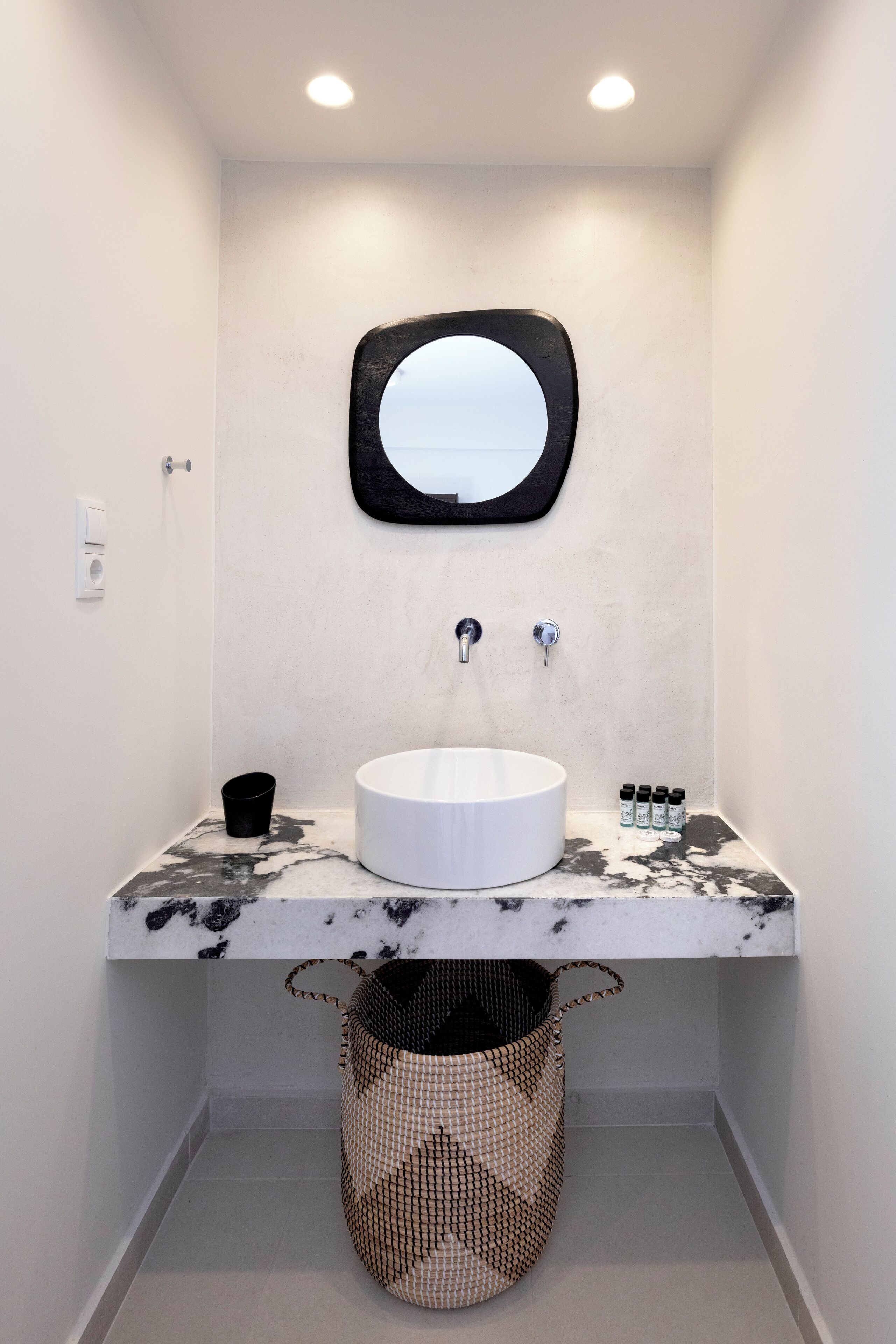 Un baño con un lavabo blanco, un espejo con marco negro y una cesta de mimbre.