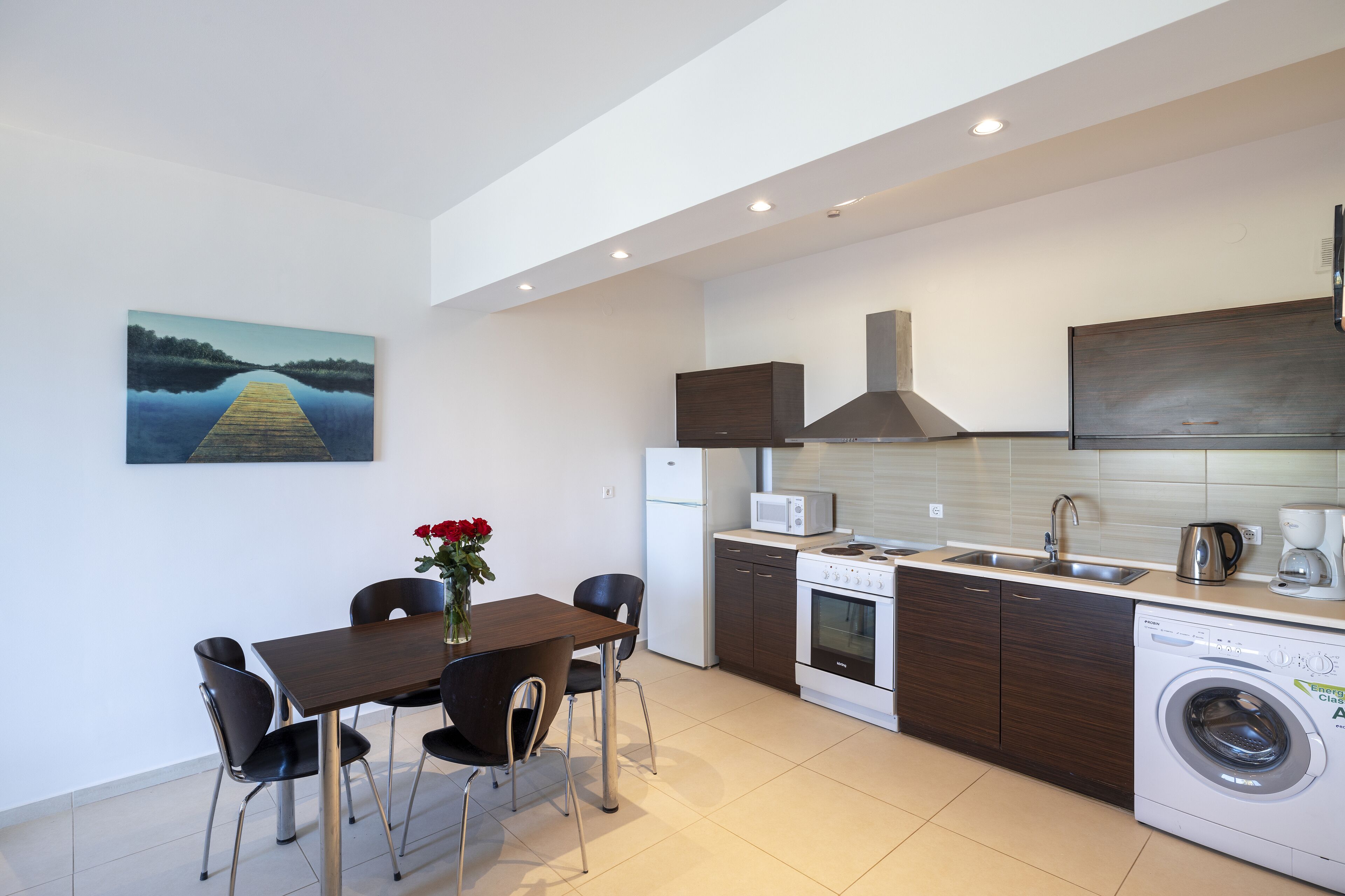 A modern kitchen with a dining area, including a table with chairs, a microwave, a coffee maker, and a washing machine.