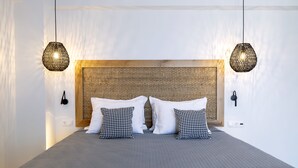 A neatly made bed with a grey quilt, two white pillows, and two black and white patterned pillows. There are two hanging wicker lamps on either side of the bed. - La Stella Suites (Rethymno)