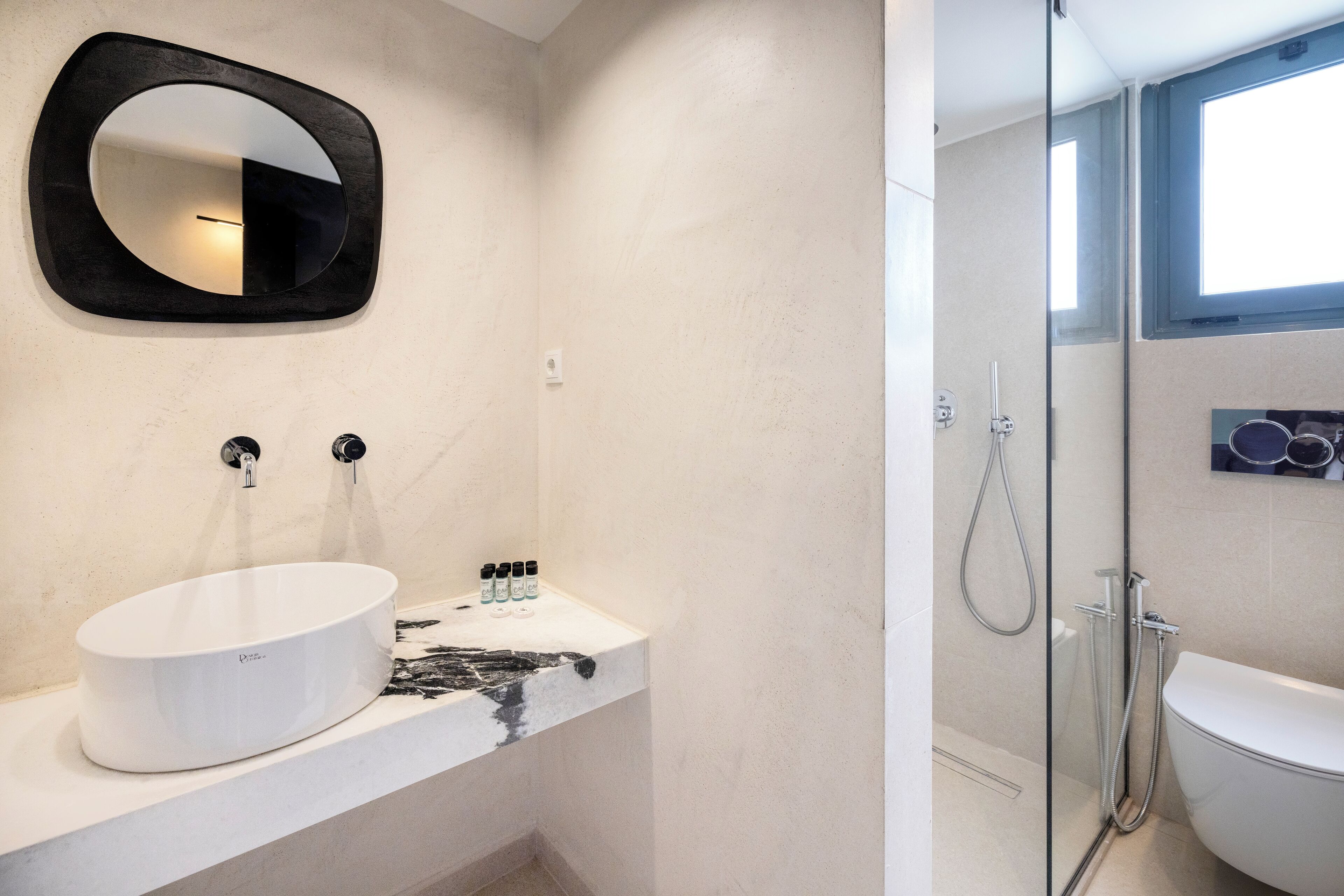 A modern bathroom with a white sink, black and white marble countertop, a large mirror, and a glass-enclosed shower.