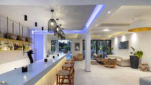 A modern bar area with a long counter, wicker chairs, and a seating area with sofas and a coffee table. - La Stella Suites (Rethymno)
