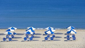 A beach with rows of blue and white beach umbrellas and lounge chairs. - La Stella Suites (Rethymno)
