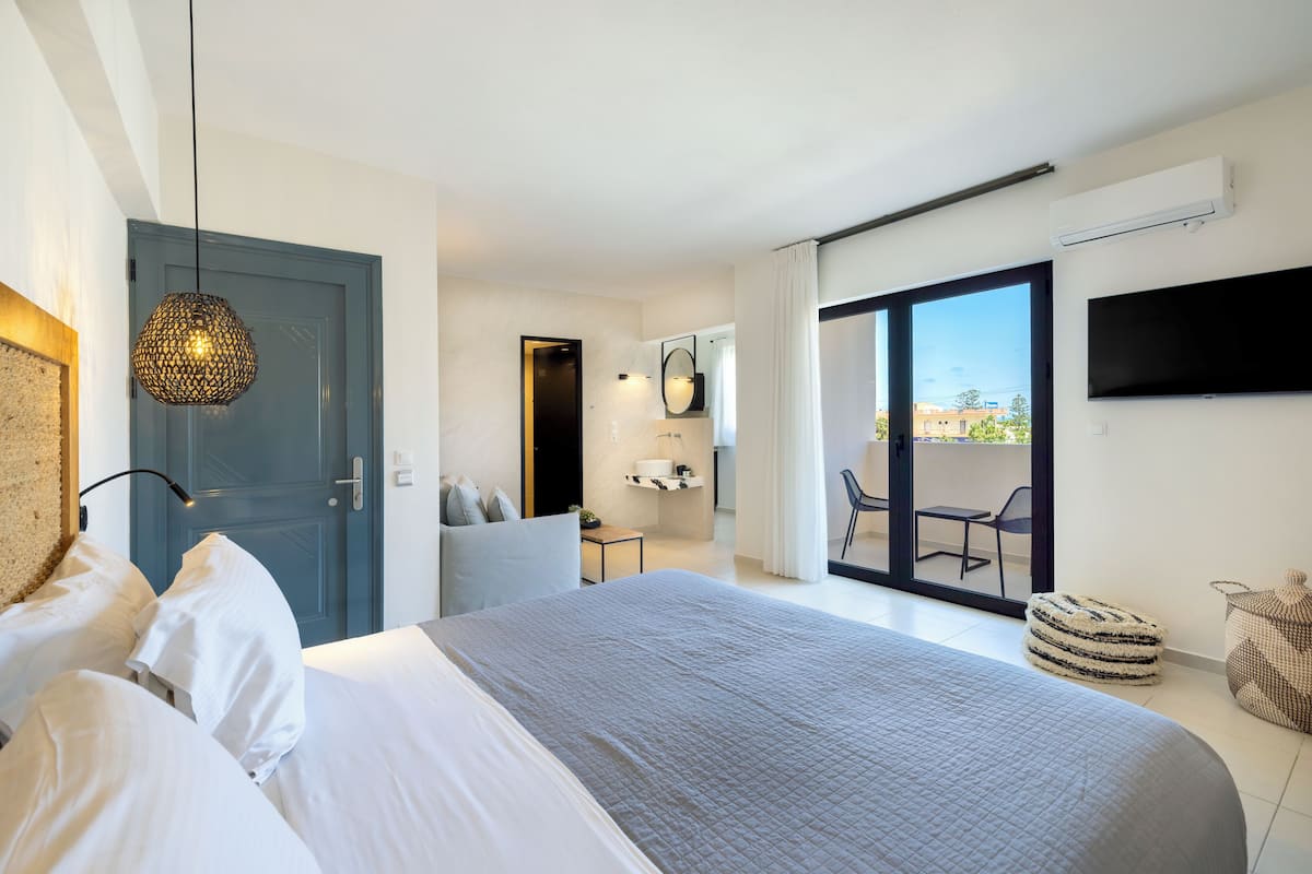Quarto moderno com cama grande, luminária no teto, televisão e varanda com cadeira.