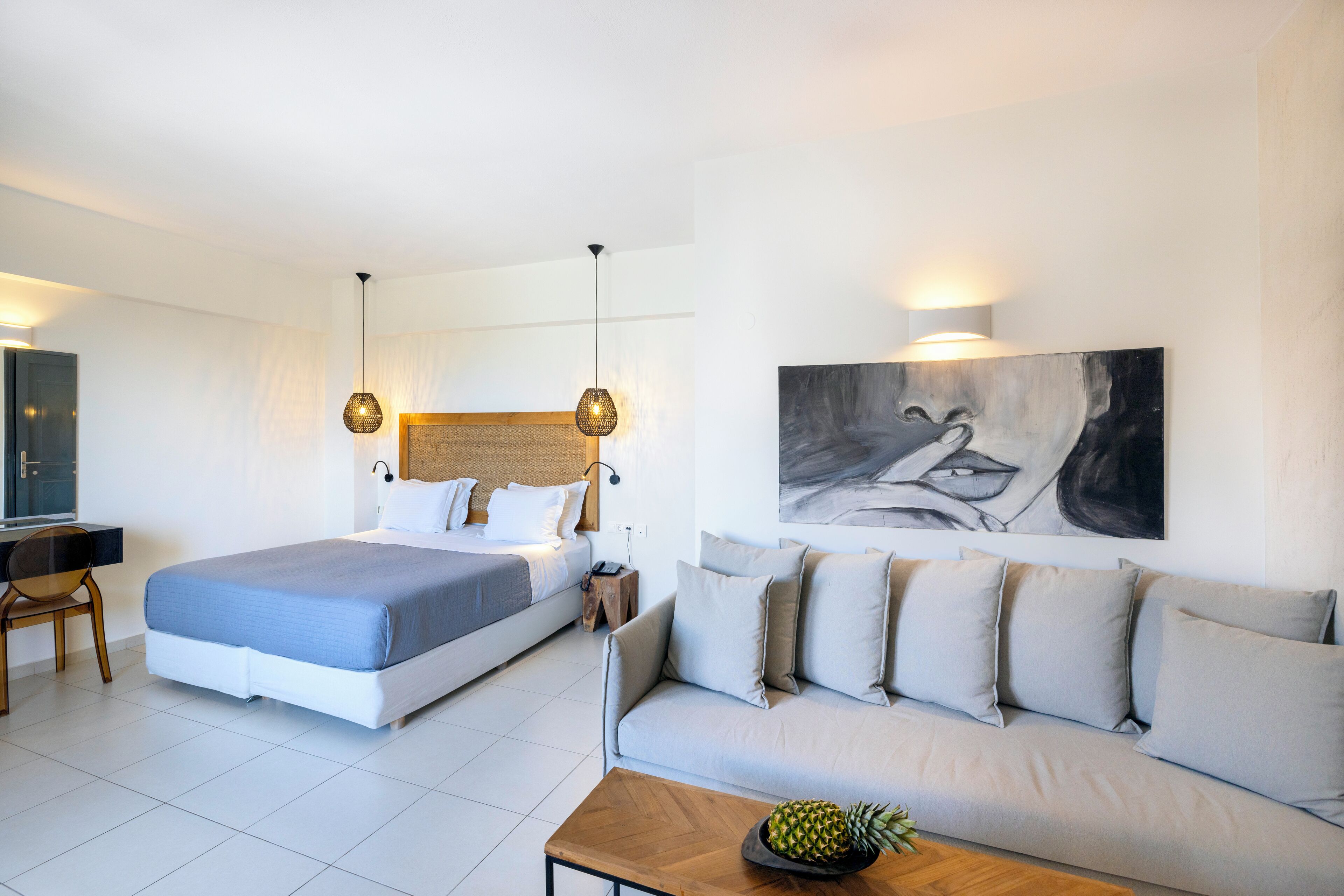 A modern hotel room with a bed, sofa, and a painting on the wall.