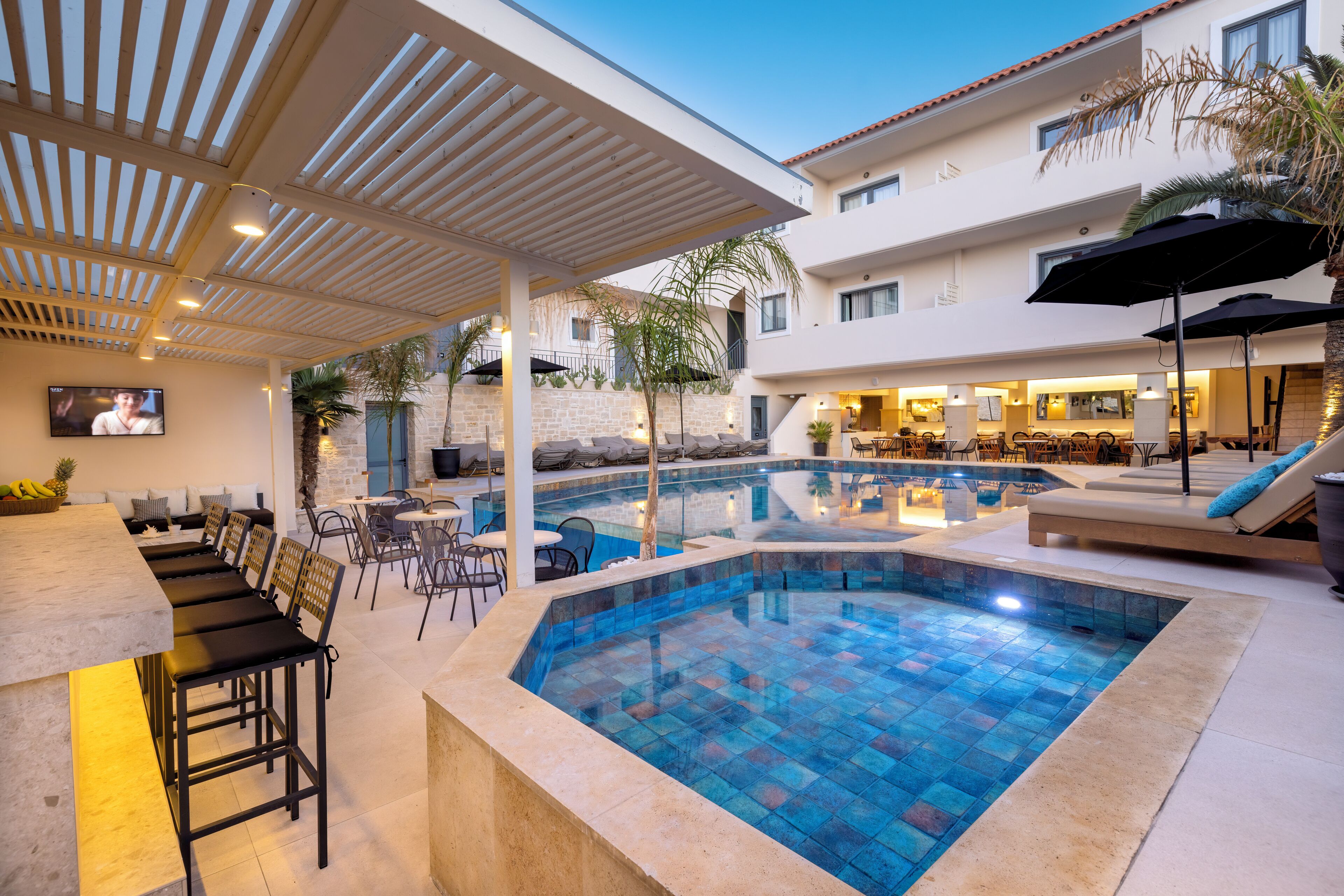 A modern outdoor pool area with a bar, seating, and a restaurant.