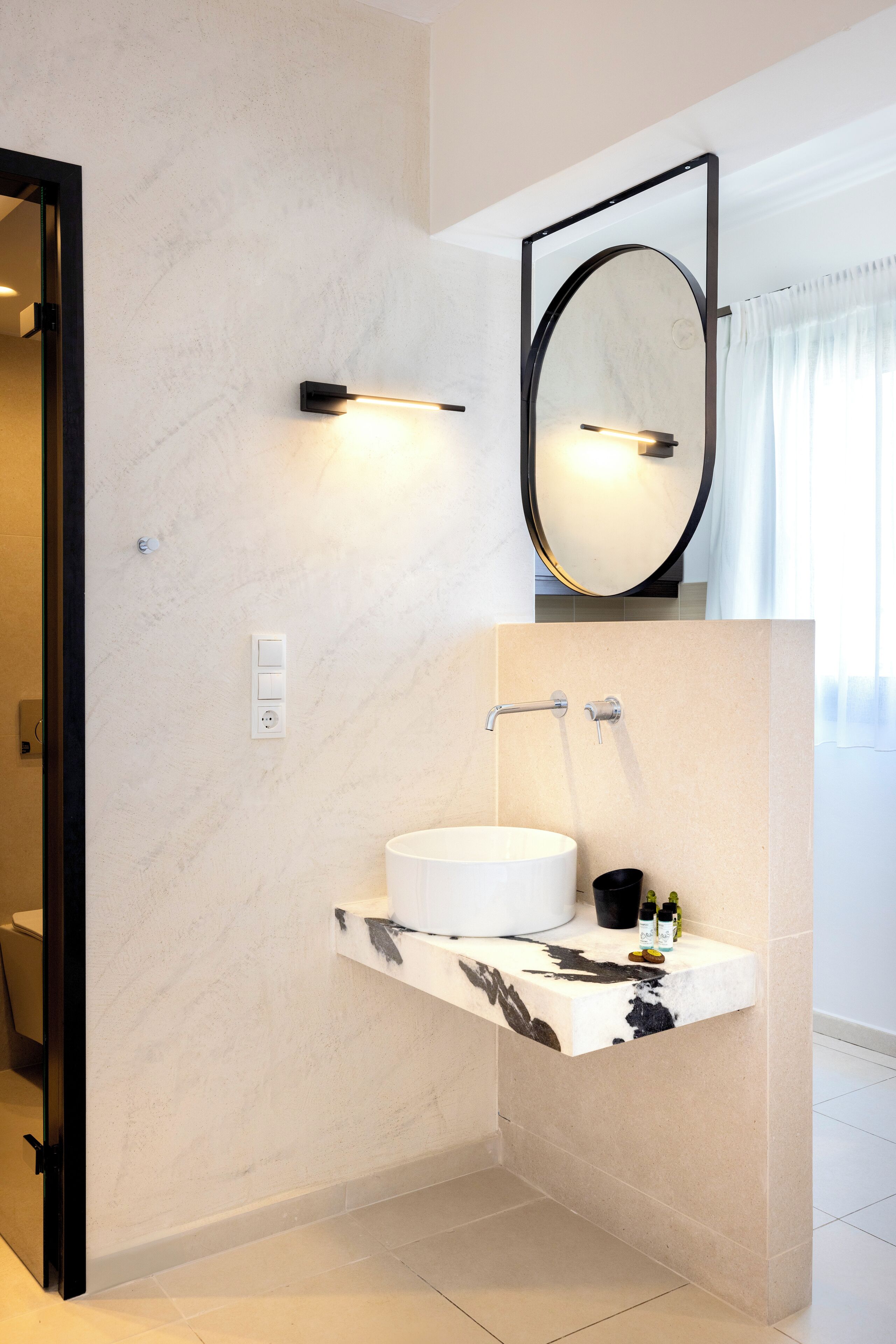 Une salle de bain moderne avec un meuble-lavabo en marbre, un grand miroir et un luminaire fixé au mur.