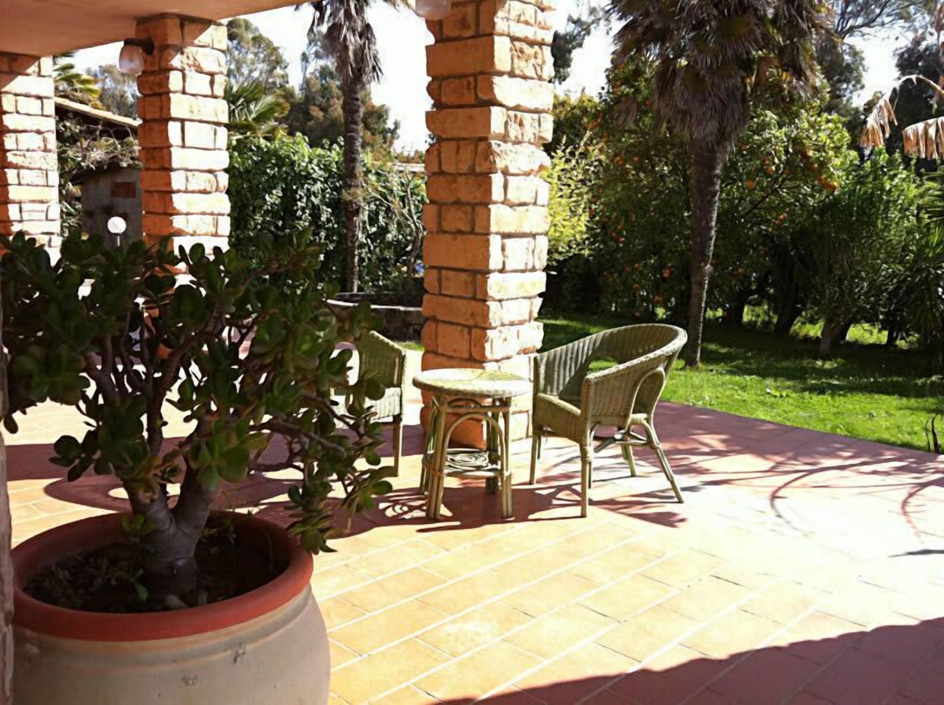 A patio area with a brick column, a potted plant, a wicker chair, and a small table.