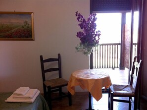 A room with a bed, a chair, a table with a vase of flowers, and a painting on the wall. - Agriturismo Agave (Alghero)