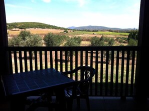 A balcony with a table and chair, overlooking a landscape with fields and hills. - Agriturismo Agave (Alghero)