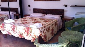 A bedroom with a large bed, two nightstands, a green wicker chair, and two paintings on the wall. - Agriturismo Agave (Alghero)