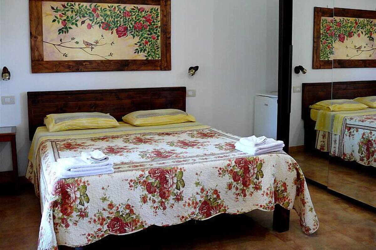 A bedroom with a wooden headboard, floral bedspread, and a painting of a branch with flowers.