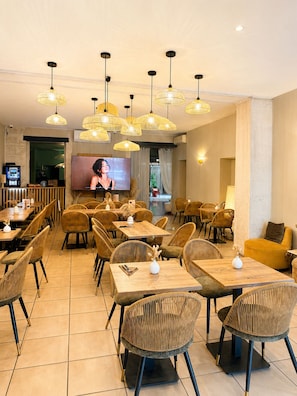Un restaurante con varias mesas y sillas, una pantalla de televisión y lámparas colgantes.