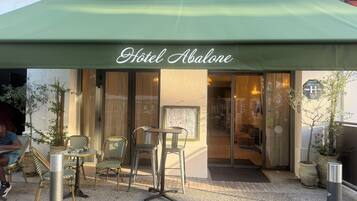 A hotel entrance with a green awning, outdoor seating, and a sign reading 'Hotel Abalone.'
