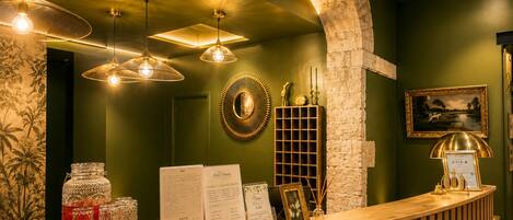 Un espace d’accueil avec un comptoir de réception en bois, des lampes suspendues, un miroir fixé au mur et un tableau encadré.