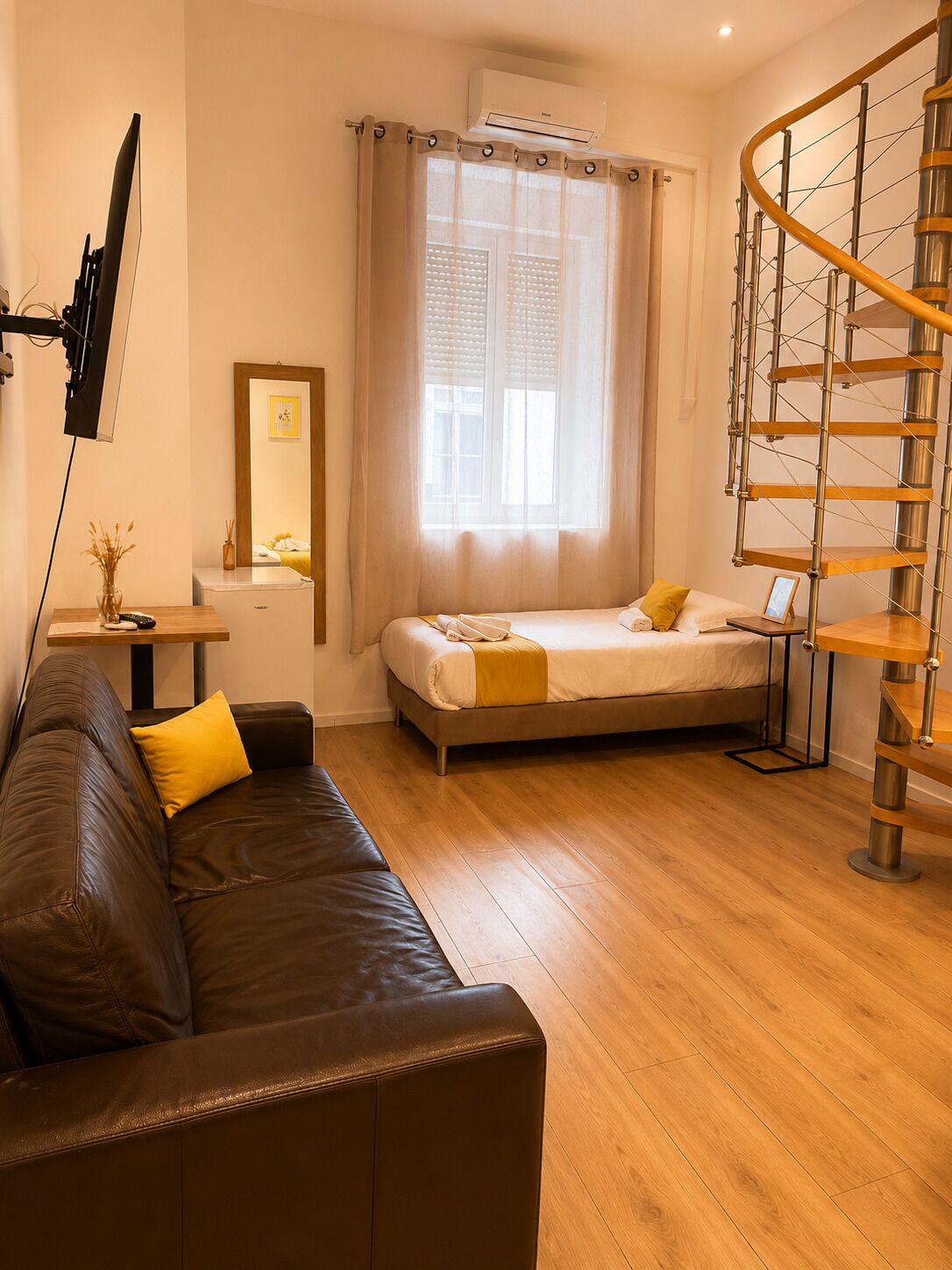 Una camera da letto moderna con un letto, un divano in pelle marrone, un pavimento in legno, una scala a chiocciola e un'ampia finestra con tende.