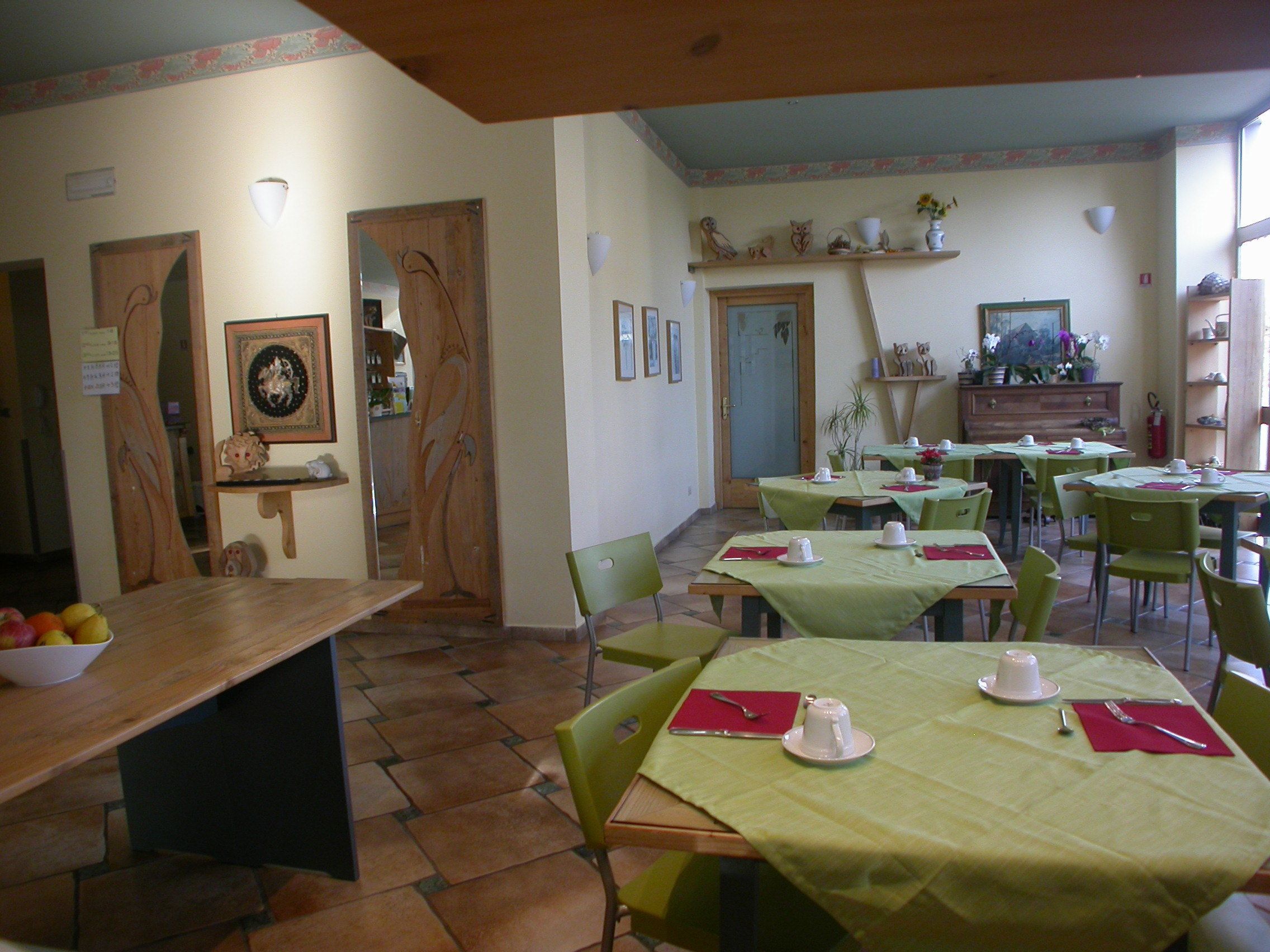 A dining area with multiple tables and chairs, a wooden buffet table with fruits, and a door leading to another room.