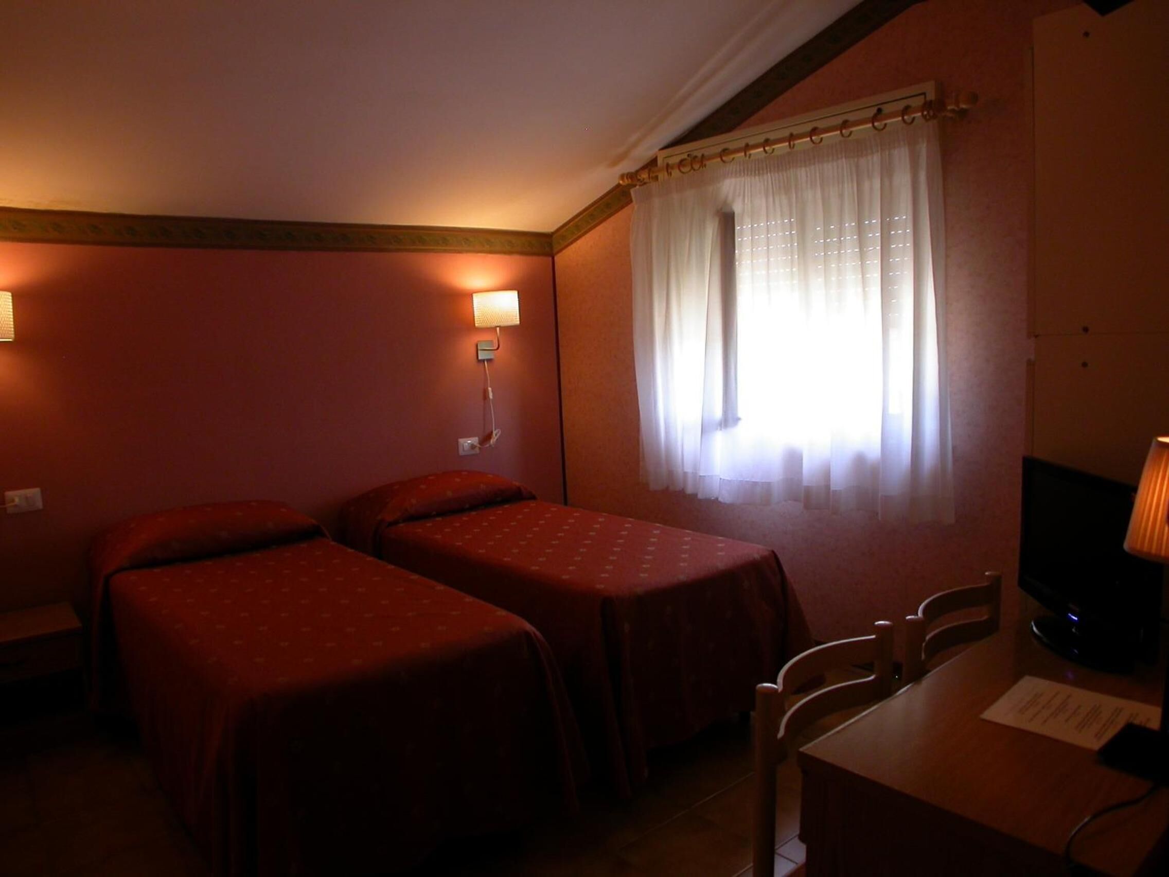 Une chambre d’hôtel avec deux lits simples, un bureau avec une chaise, une télévision et une fenêtre avec des rideaux.
