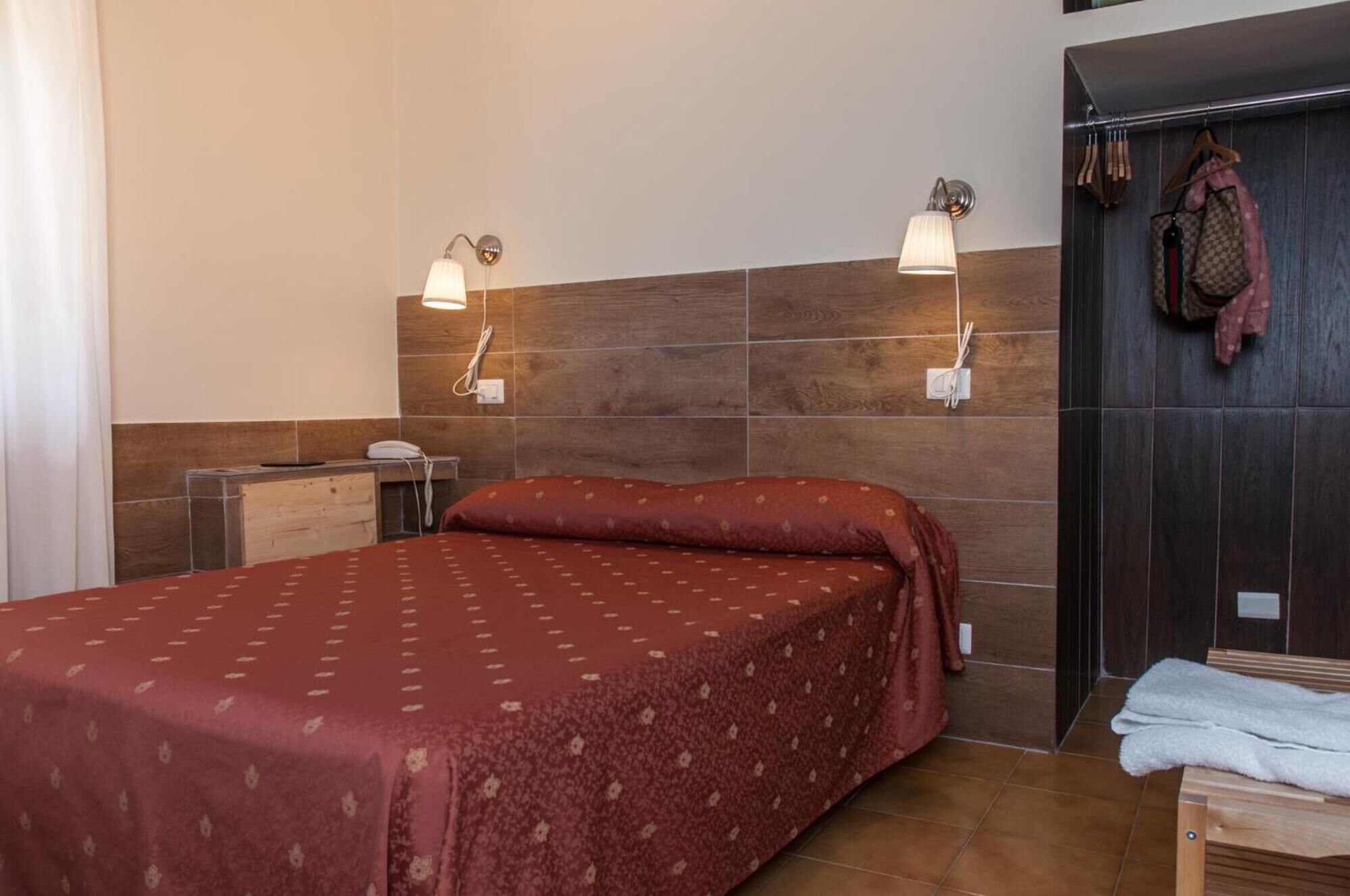 A hotel room with a bed, bedside lamps, a wooden desk, and a wardrobe.
