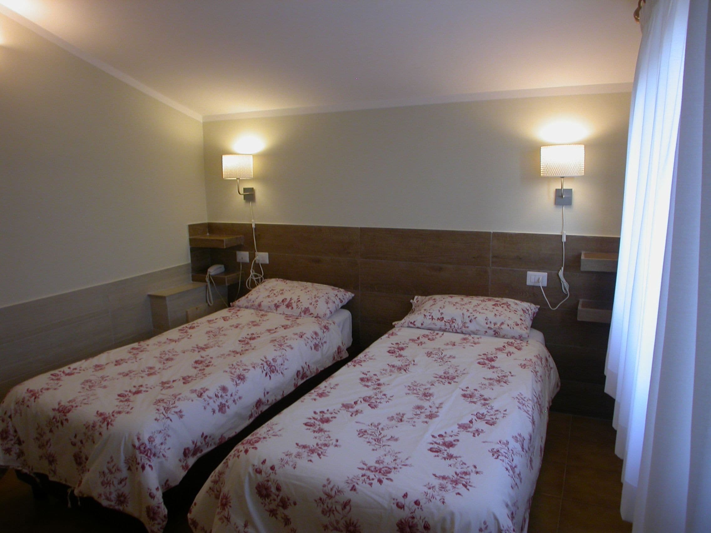 Une chambre d’hôtel avec deux lits simples, chacun agrémenté d’une couvre-lit à motifs floraux, d’une table de chevet et d’une lampe fixée au mur.