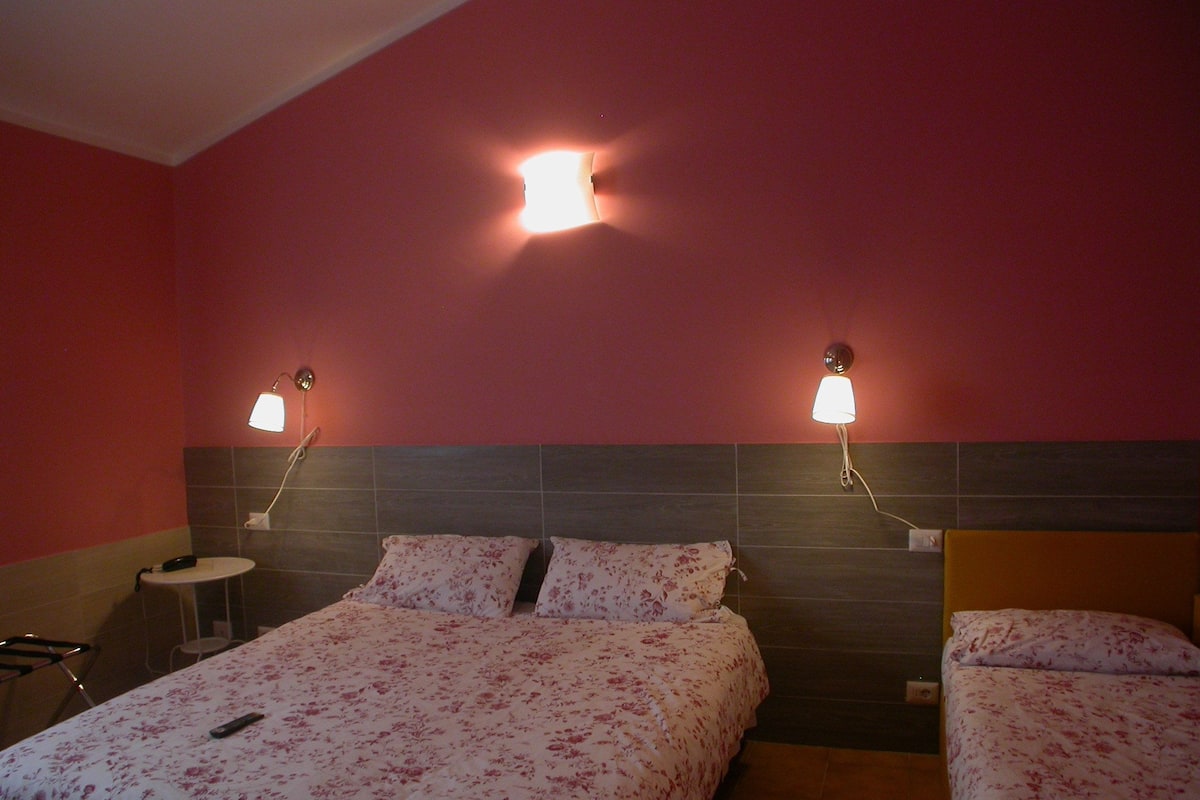 A hotel room with two beds, each with floral bedding, a small bedside table, and a wall-mounted lamp.