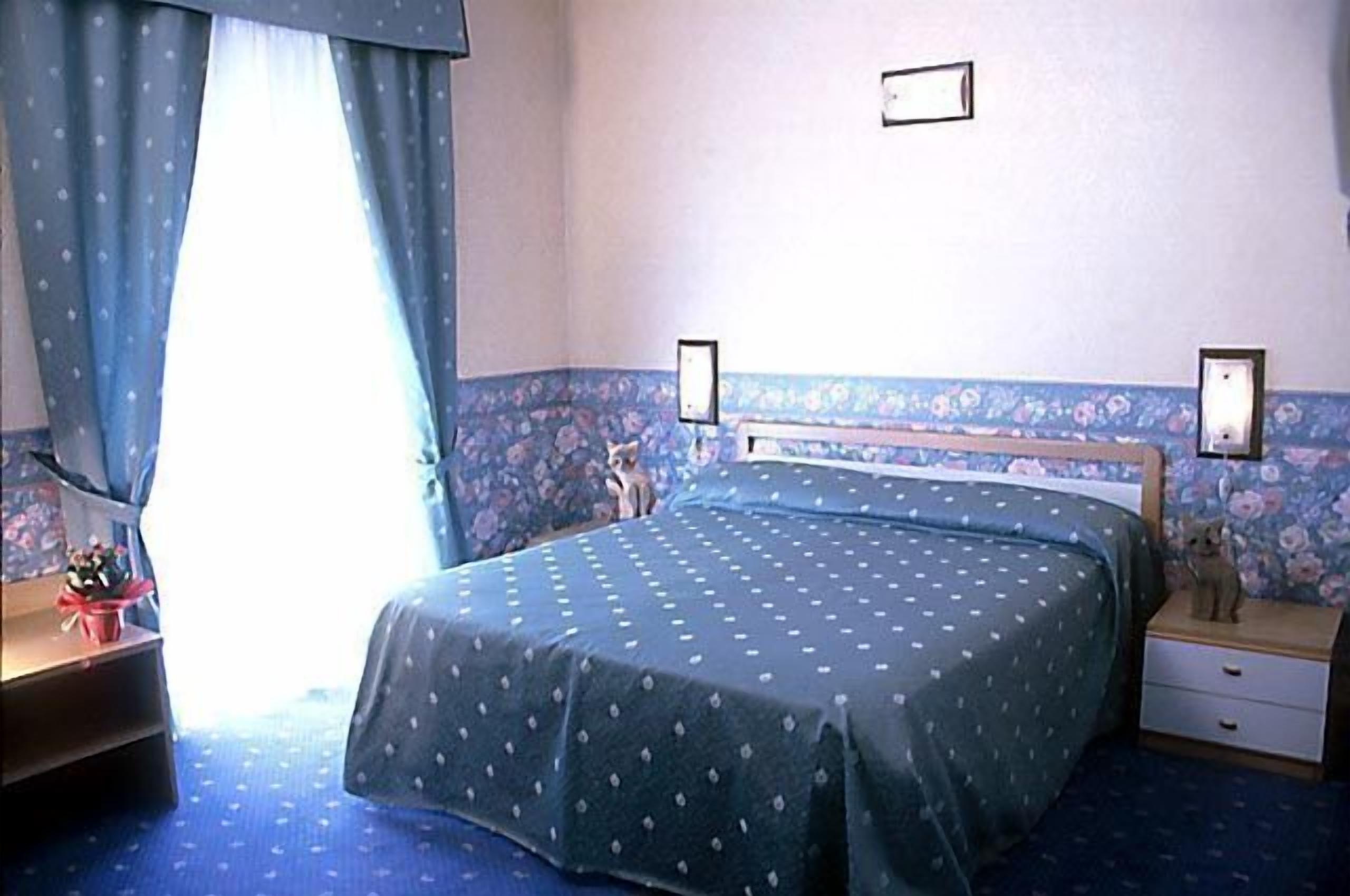 Una camera da letto con un letto, un comodino, una cassettiera e una finestra con tende.