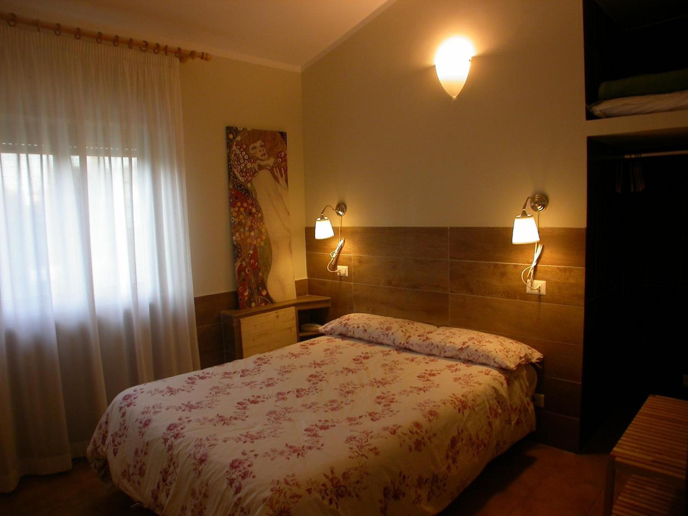 A hotel room with a bed, two bedside lamps, a painting on the wall, and a window with curtains.