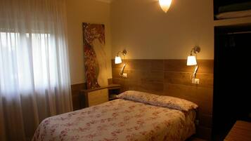 Habitación de hotel con una cama, dos lámparas de noche, un cuadro en la pared y una ventana con cortinas.