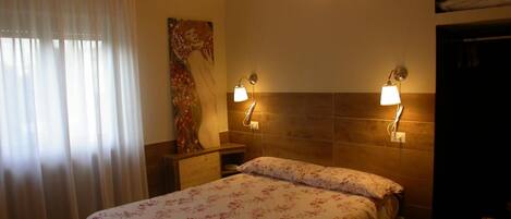A hotel room with a bed, two bedside lamps, a painting on the wall, and a window with curtains.