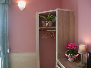 Una habitación de esquina con un mueble de madera, una planta colgante, una lámpara y una ventana con cortina.