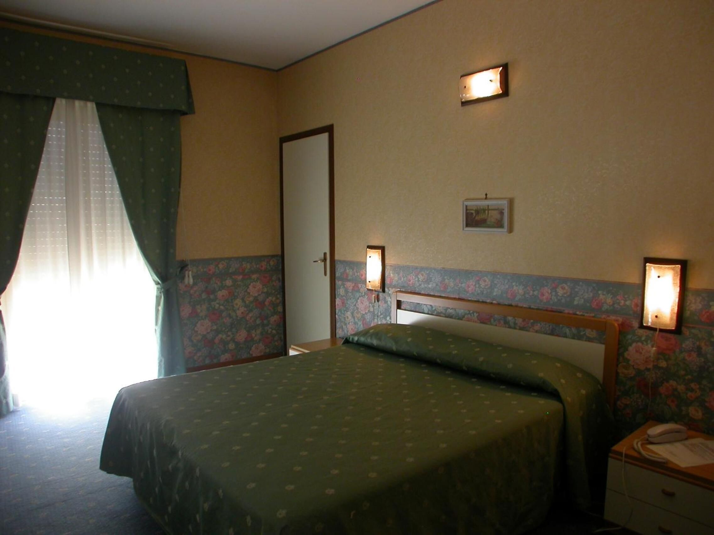 Ett hotellrum med en säng, ett nattduksbord och en dörr.