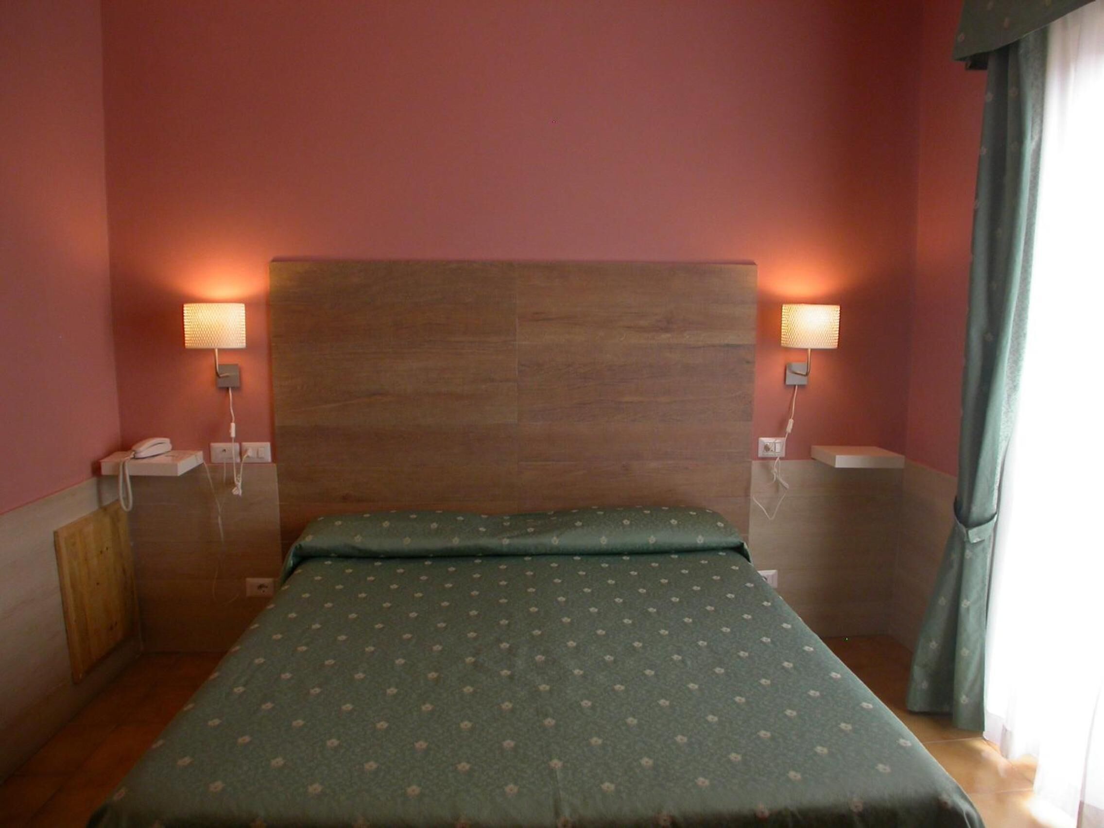 A single-bed room with a wooden headboard, two bedside lamps, and a green bedspread.