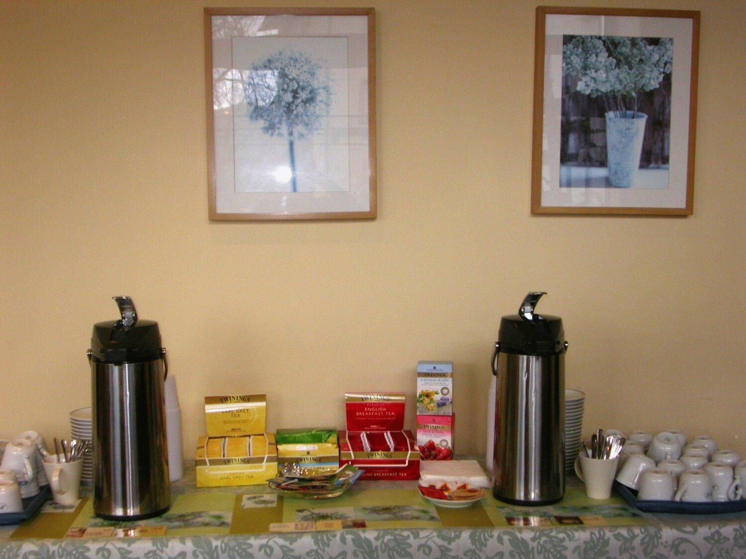 A breakfast buffet setup with two coffee makers, tea boxes, and a variety of breakfast items on a table.