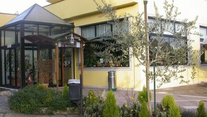 Entrada de un hotel con toldo de vidrio, un letrero que dice "HOTEL IL ROSCIO" y un pequeño jardín con plantas y flores.