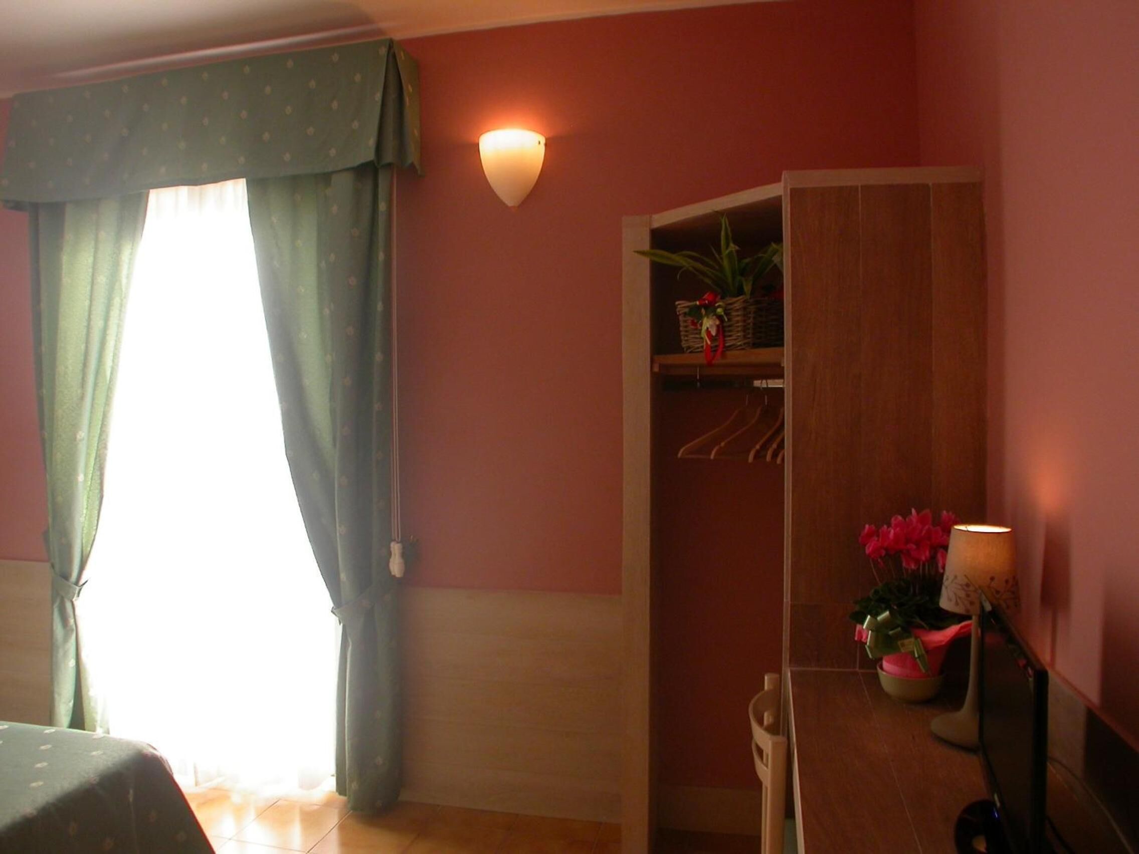 Ein Zimmer mit einem Bett, einem an der Wand befestigten Regal mit Korb und Pflanze, einer Wandleuchte und einem Fenster mit Vorhängen.