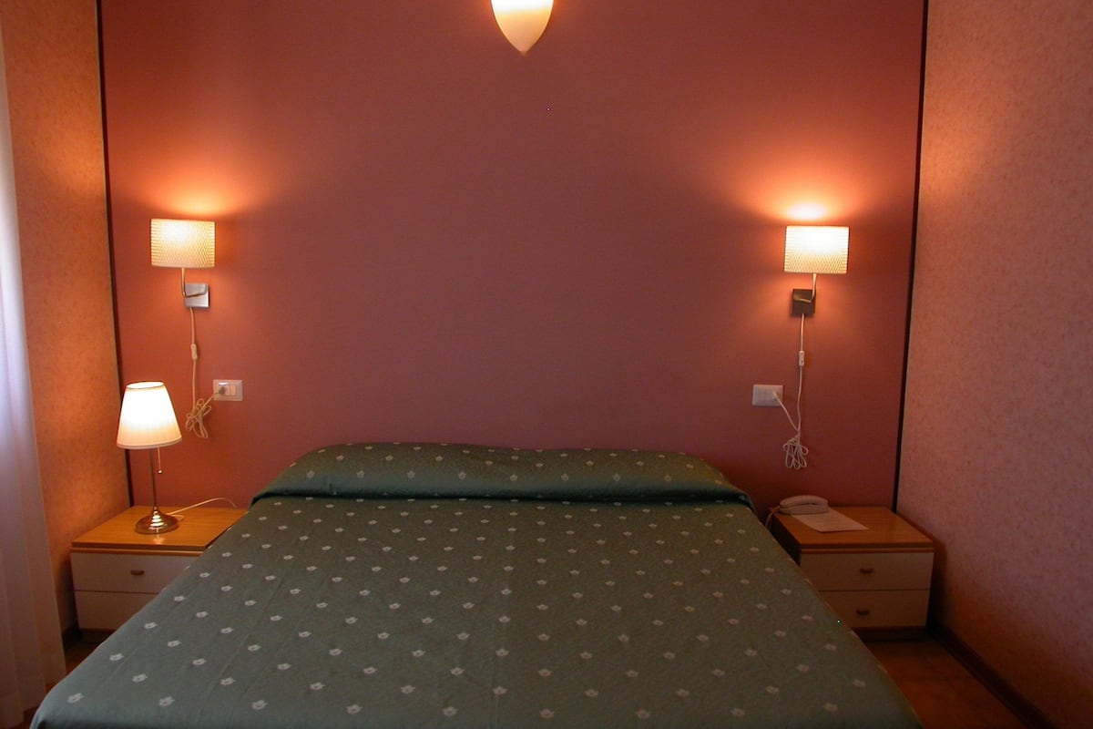 A hotel room with a bed, two bedside tables, and two wall-mounted lamps.