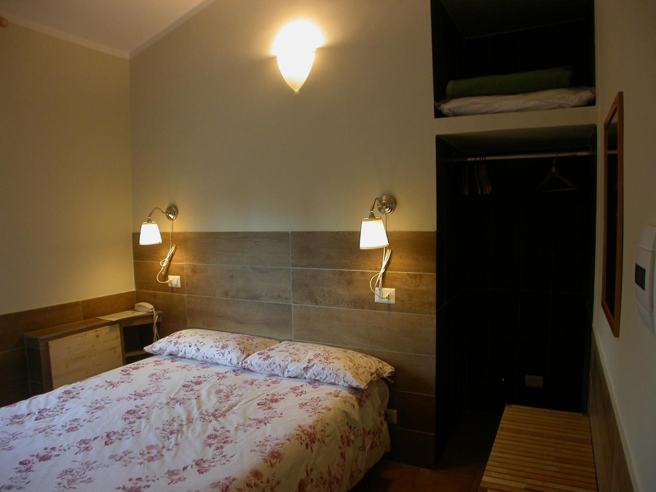 Een hotelkamer met een bed, twee wandlampen, een telefoon en een houten bankje.