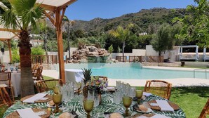 An outdoor dining area with a pool view, tables set with glassware and plates, and a tropical backdrop. - La Torre (Tarifa)